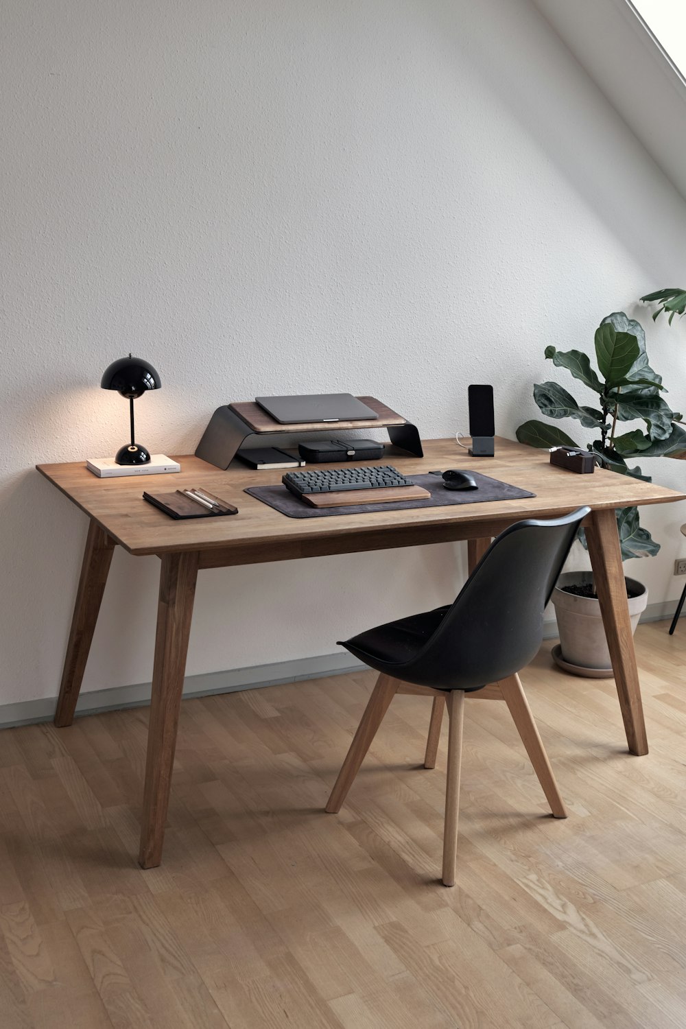 An organized home workspace with a lamp, laptop stand, keyboard, and desk accessories